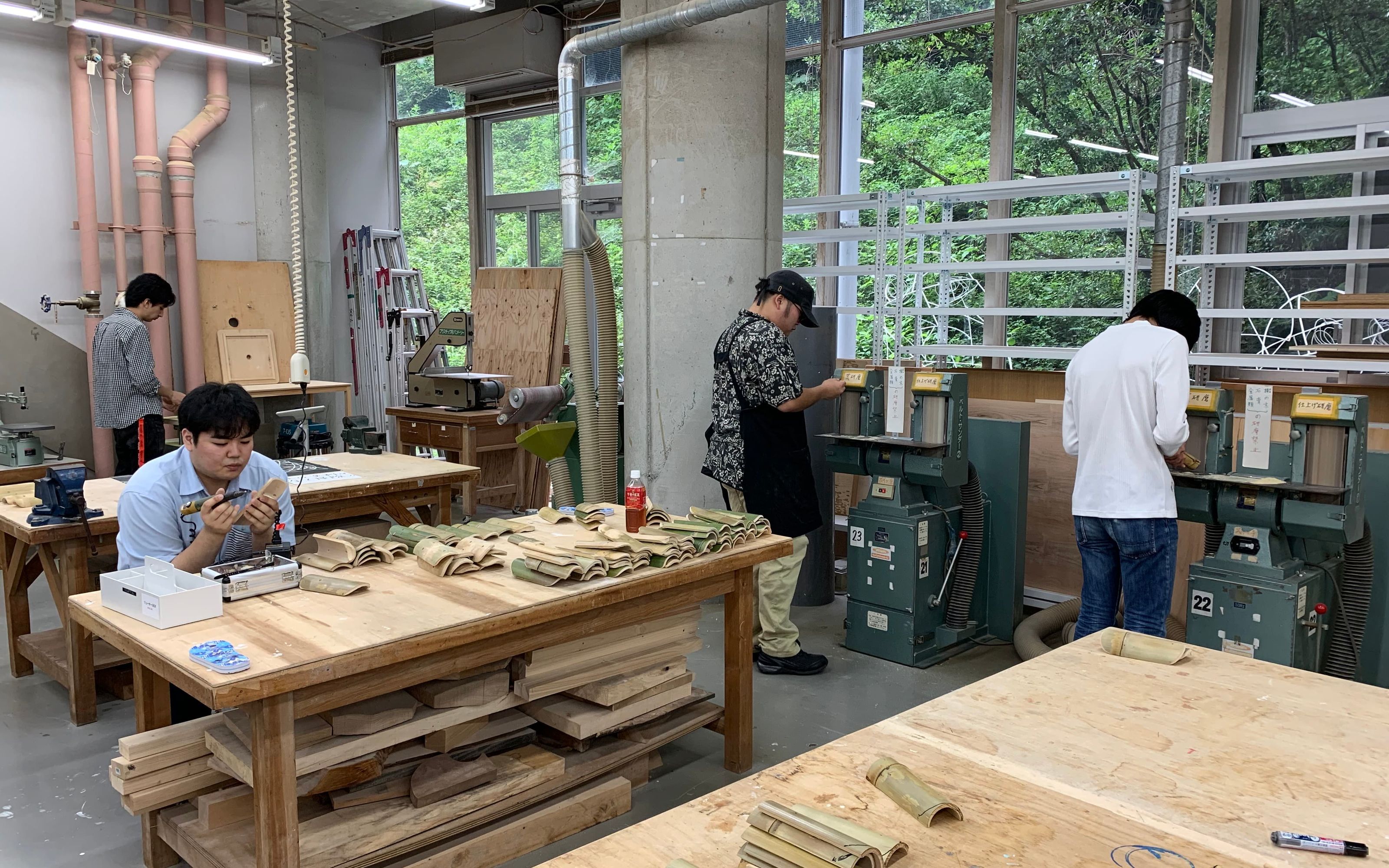 Students gathered around a workshop table covered in curved bamboo pieces and sketches, discussing the shape of bamboo sandals.