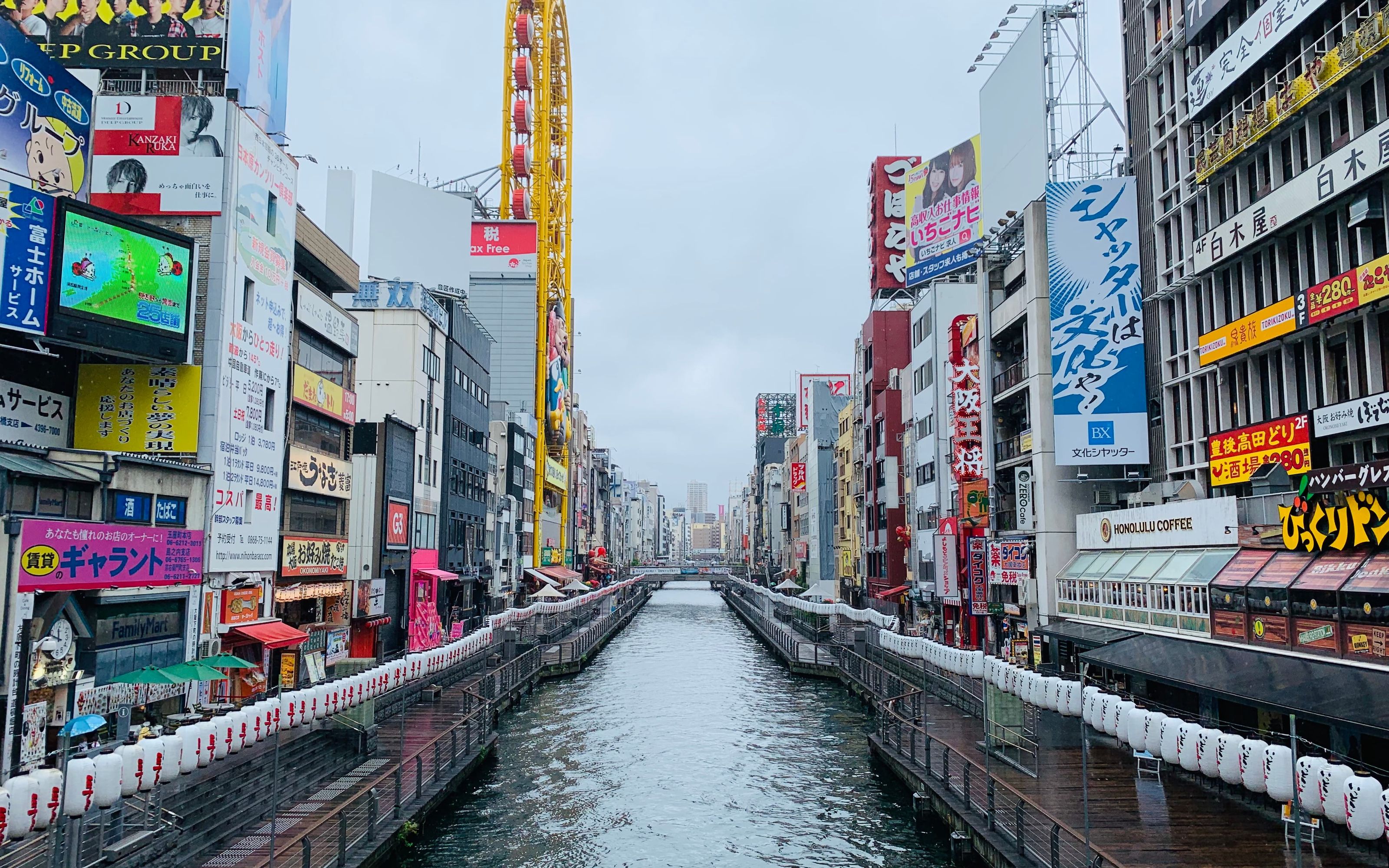 Street in Osaka lined with bright neon signs, with the Tsutenkaku tower visible in the background.